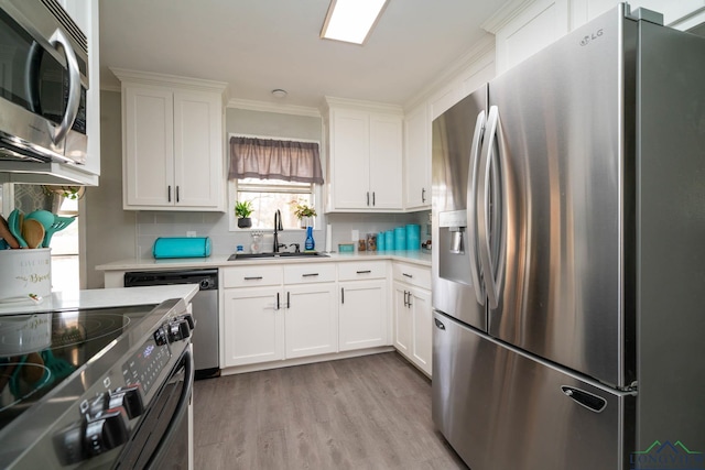 kitchen with light wood-type flooring, a sink, appliances with stainless steel finishes, white cabinets, and light countertops