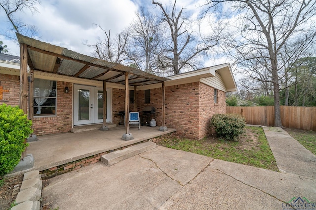 rear view of property featuring brick siding, french doors, and fence