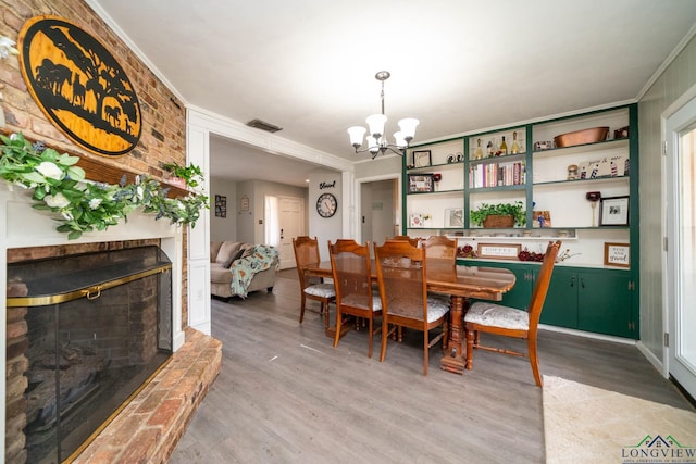 dining room featuring visible vents, a notable chandelier, light wood-style floors, a fireplace, and crown molding