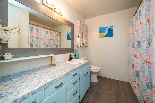 full bath with toilet, wood finished floors, vanity, and a textured wall