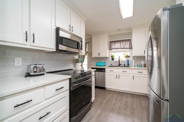 kitchen featuring white cabinets, appliances with stainless steel finishes, light wood-style flooring, and a sink