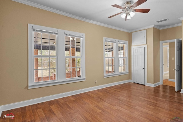 empty room with a wealth of natural light, ornamental molding, wood finished floors, and visible vents