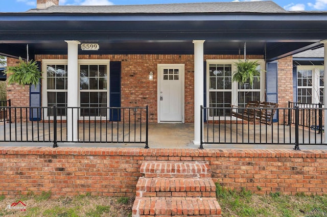 view of exterior entry featuring a shingled roof, a porch, and brick siding