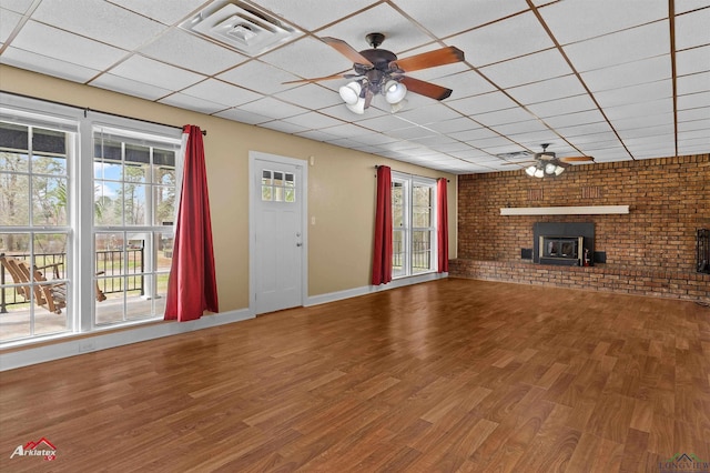 unfurnished living room featuring a paneled ceiling, visible vents, ceiling fan, brick wall, and wood finished floors