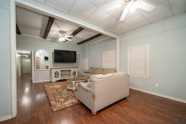 living room featuring beamed ceiling, dark hardwood / wood-style floors, a drop ceiling, and ceiling fan