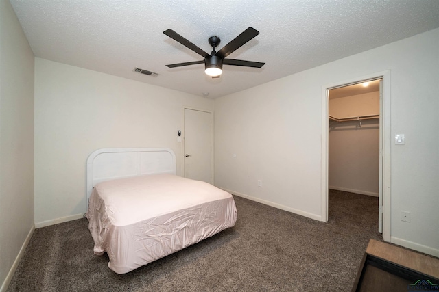 bedroom with ceiling fan, a spacious closet, a textured ceiling, and dark carpet