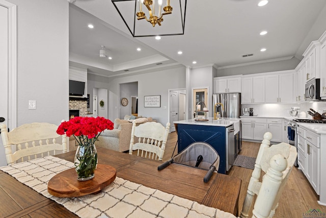 dining room with sink, a tray ceiling, a fireplace, ornamental molding, and light hardwood / wood-style floors