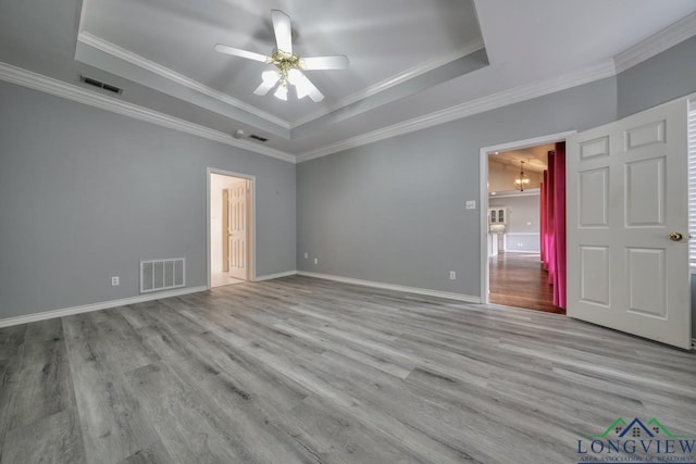 spare room featuring crown molding, ceiling fan with notable chandelier, light hardwood / wood-style floors, and a raised ceiling