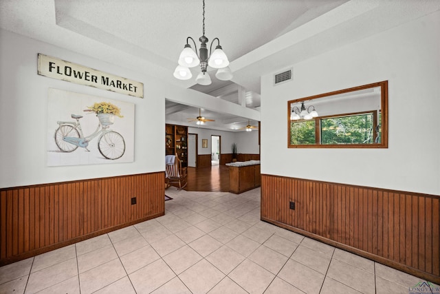 unfurnished dining area with wooden walls, ceiling fan with notable chandelier, light tile patterned flooring, and a textured ceiling