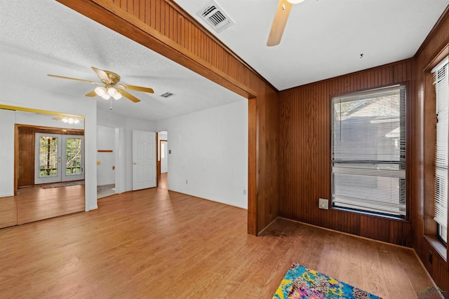 interior space featuring french doors, a textured ceiling, ceiling fan, light hardwood / wood-style flooring, and wood walls