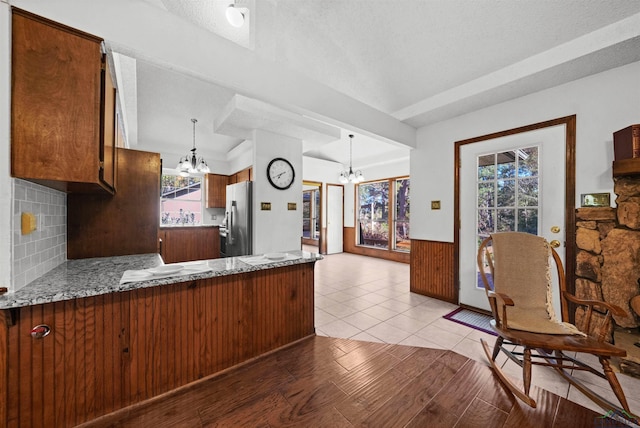 kitchen with kitchen peninsula, stainless steel fridge, light stone countertops, decorative light fixtures, and an inviting chandelier