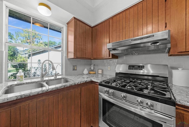 kitchen with backsplash, light stone counters, gas stove, sink, and range hood