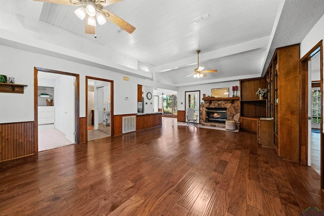 unfurnished living room featuring hardwood / wood-style flooring, ceiling fan, wood walls, and a stone fireplace