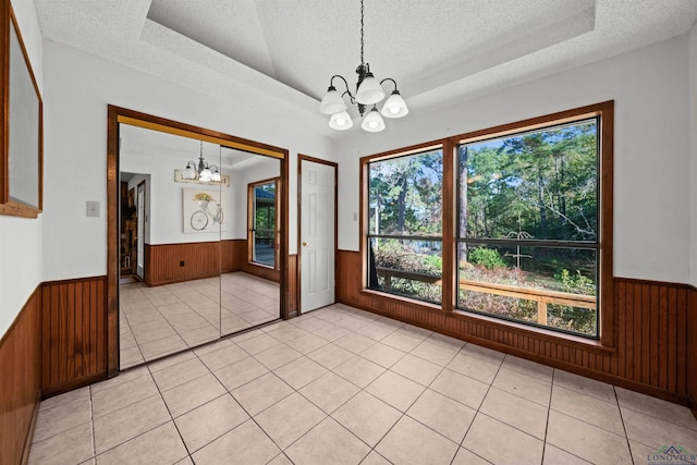 unfurnished dining area with a raised ceiling, light tile patterned floors, a textured ceiling, and a notable chandelier