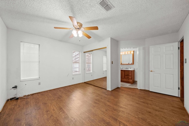 unfurnished bedroom featuring ensuite bath, ceiling fan, a textured ceiling, a closet, and hardwood / wood-style flooring