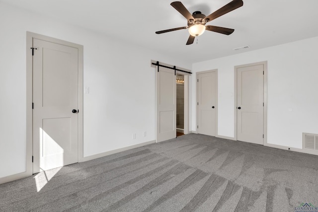 unfurnished bedroom featuring multiple closets, a barn door, light carpet, and ceiling fan