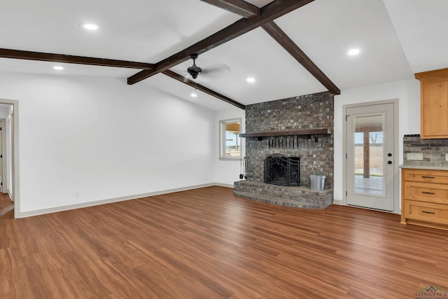 unfurnished living room with vaulted ceiling with beams, a wealth of natural light, hardwood / wood-style floors, and a brick fireplace