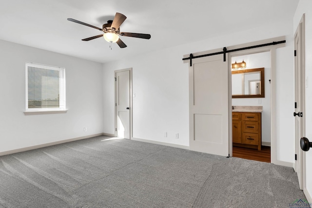 unfurnished bedroom featuring ceiling fan, carpet flooring, a barn door, and ensuite bath