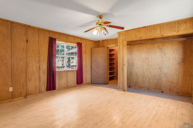 unfurnished bedroom featuring ceiling fan, light hardwood / wood-style floors, a textured ceiling, and wooden walls