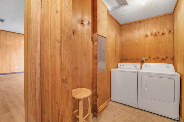 clothes washing area with wood walls, independent washer and dryer, a textured ceiling, and electric panel