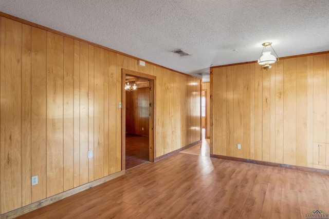 unfurnished room with hardwood / wood-style floors, a textured ceiling, and wooden walls