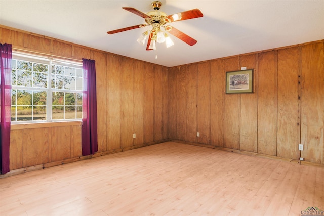 unfurnished room with light hardwood / wood-style flooring, ceiling fan, and wood walls