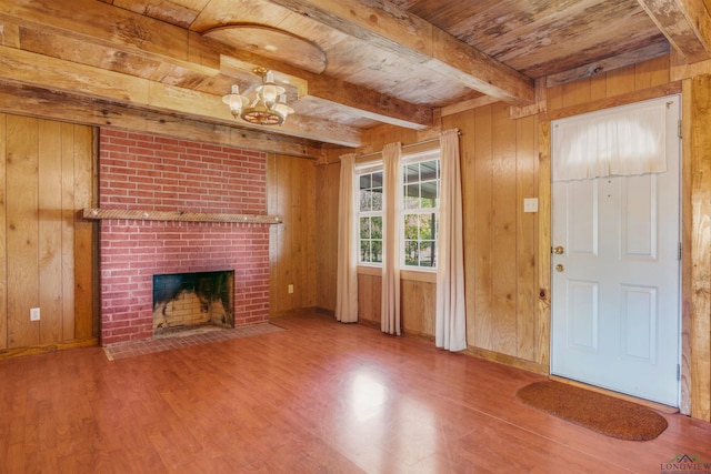 unfurnished living room featuring a brick fireplace, wooden walls, beam ceiling, an inviting chandelier, and wooden ceiling