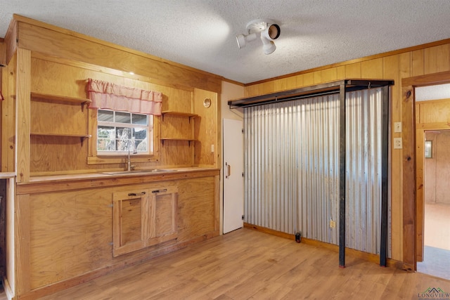 kitchen with sink, light hardwood / wood-style flooring, wood walls, crown molding, and a textured ceiling