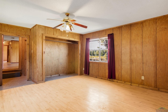 unfurnished bedroom with ceiling fan, light wood-type flooring, wooden walls, and a closet