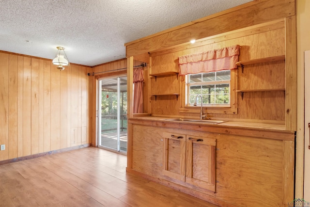 kitchen featuring pendant lighting, wood walls, sink, light wood-type flooring, and a textured ceiling