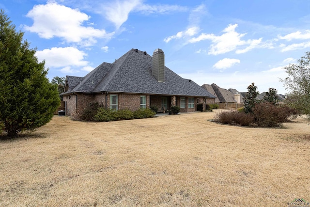 view of front facade with roof with shingles, brick siding, a chimney, and a front yard