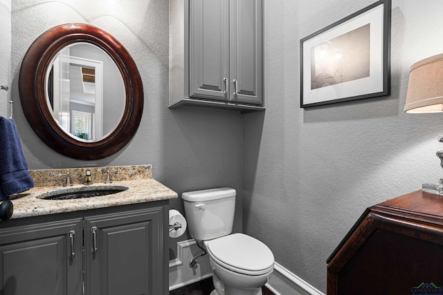 half bathroom with toilet, vanity, baseboards, and a textured wall