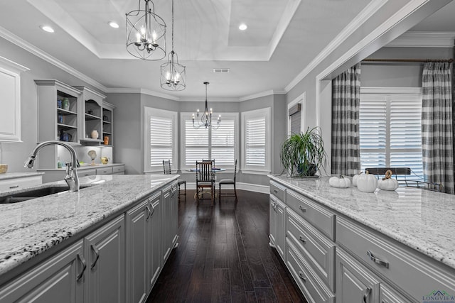 kitchen featuring a tray ceiling, gray cabinetry, dark wood-type flooring, a sink, and a chandelier