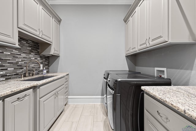 laundry area featuring crown molding, cabinet space, a sink, independent washer and dryer, and baseboards