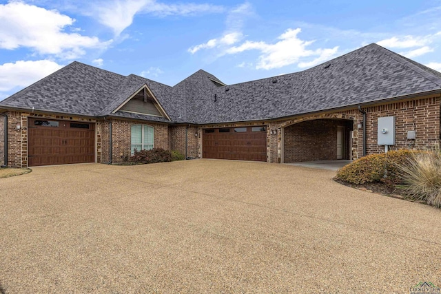 view of front facade with an attached garage, brick siding, and a shingled roof