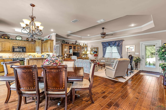 dining room featuring wood-type flooring, ceiling fan with notable chandelier, a tray ceiling, and ornamental molding