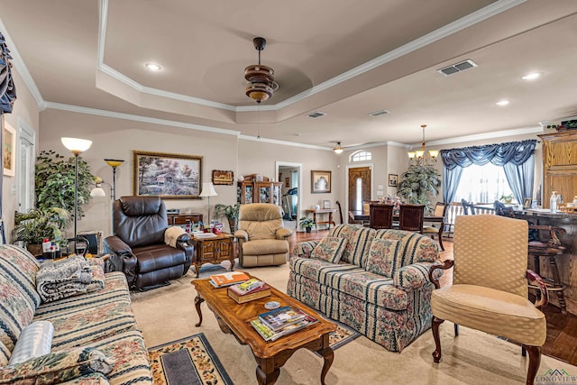 living room with a tray ceiling, ceiling fan with notable chandelier, and ornamental molding