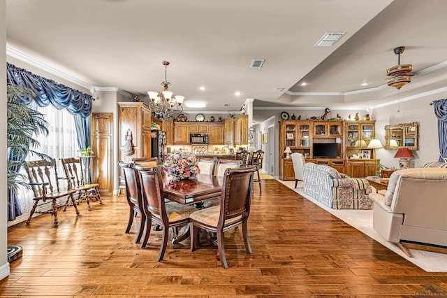 dining area with ceiling fan with notable chandelier, a raised ceiling, crown molding, and light hardwood / wood-style flooring