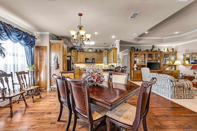 dining area featuring a raised ceiling, light wood-type flooring, ornamental molding, and a chandelier