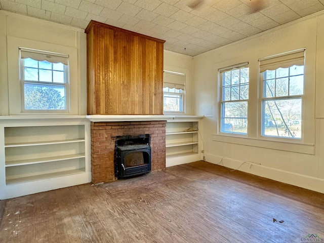 unfurnished living room with a wood stove, built in shelves, and hardwood / wood-style floors