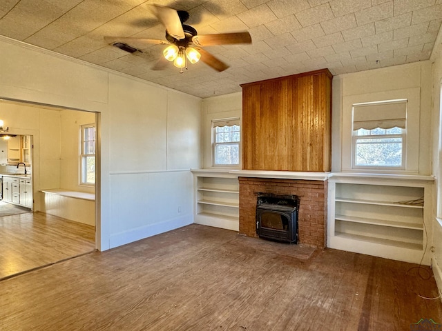 unfurnished living room featuring hardwood / wood-style flooring, sink, a wood stove, and ceiling fan