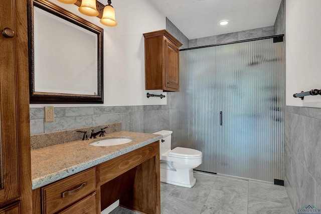 bathroom with vanity, a shower with door, tile patterned floors, toilet, and tile walls