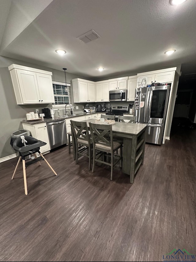 kitchen featuring appliances with stainless steel finishes, hanging light fixtures, white cabinets, and dark wood-type flooring