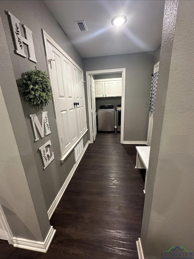 hall with dark wood-style flooring, washer and clothes dryer, visible vents, and baseboards