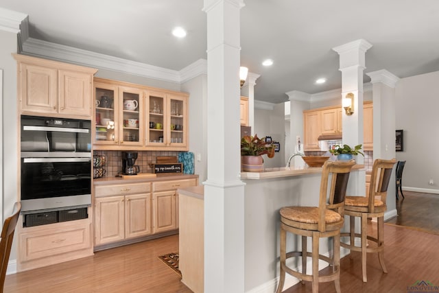 kitchen featuring a kitchen bar, decorative columns, light brown cabinets, and stainless steel double oven