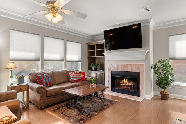 living area with visible vents, a tile fireplace, crown molding, and wood finished floors