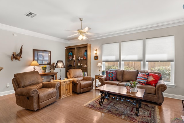 living room featuring visible vents, baseboards, light wood-type flooring, ornamental molding, and a ceiling fan