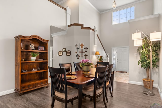 dining space featuring crown molding, wood finished floors, baseboards, and a towering ceiling