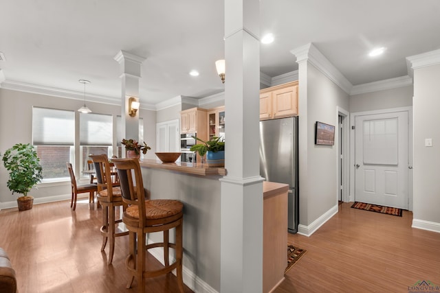 kitchen with light wood-type flooring, light brown cabinets, freestanding refrigerator, a breakfast bar area, and decorative columns