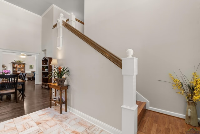 staircase with a towering ceiling, a ceiling fan, baseboards, and wood finished floors